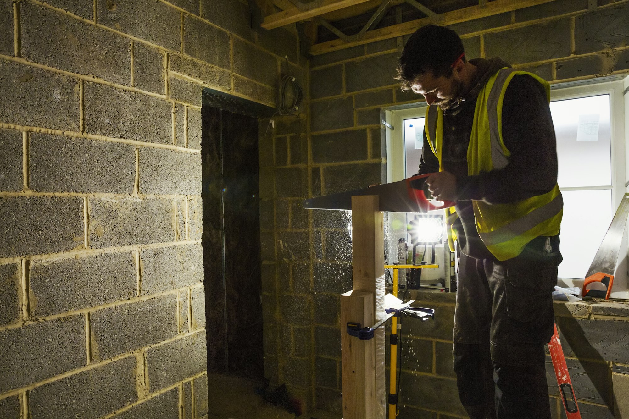 A builder on a home build site using a saw on a block of wood.